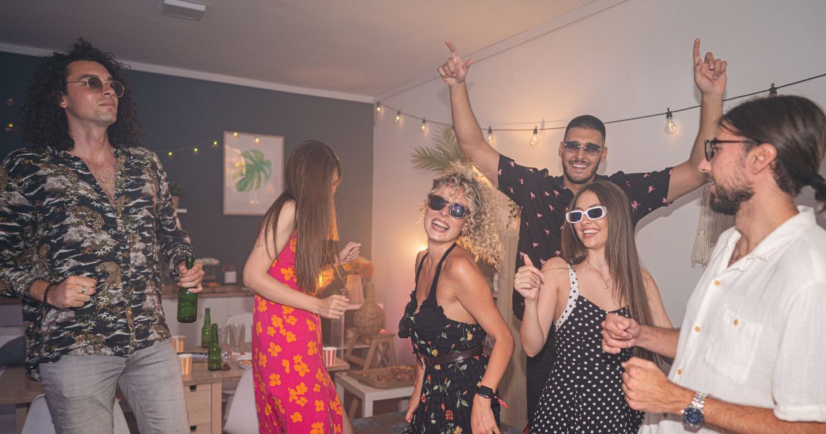 A group of young female and male friends dancing during a house party.