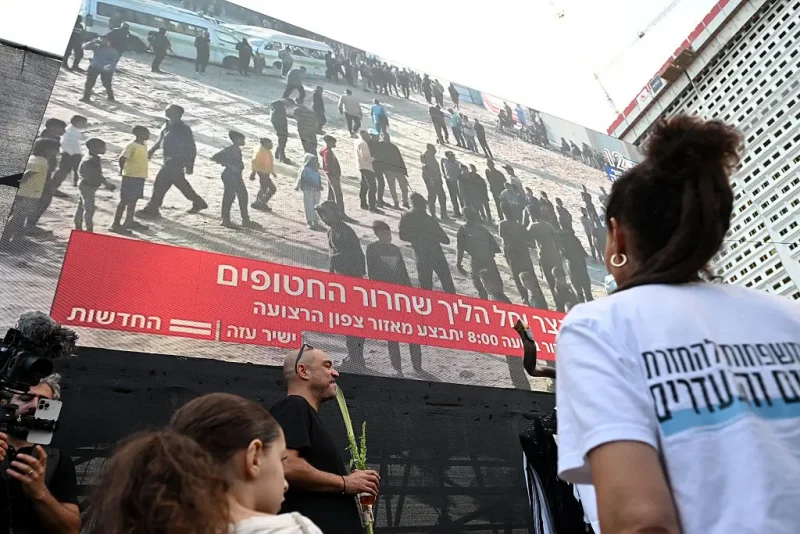 TEL AVIV, ISRAEL - OCTOBER 13: People watch a large screen broadcasting a live feed of Gaza, as they wait for the start of the hostage release at Hostages Square on October 13, 2025 in Tel Aviv, Israel. The ceasefire deal between Israel and Hamas has brought an end to the two years of war that followed the attacks of Oct. 7, 2023. A condition of the deal was the immediate return of 48 hostages held in Gaza, around 20 of whom were believed to be alive. (Photo by Alexi J. Rosenfeld/Getty Images)