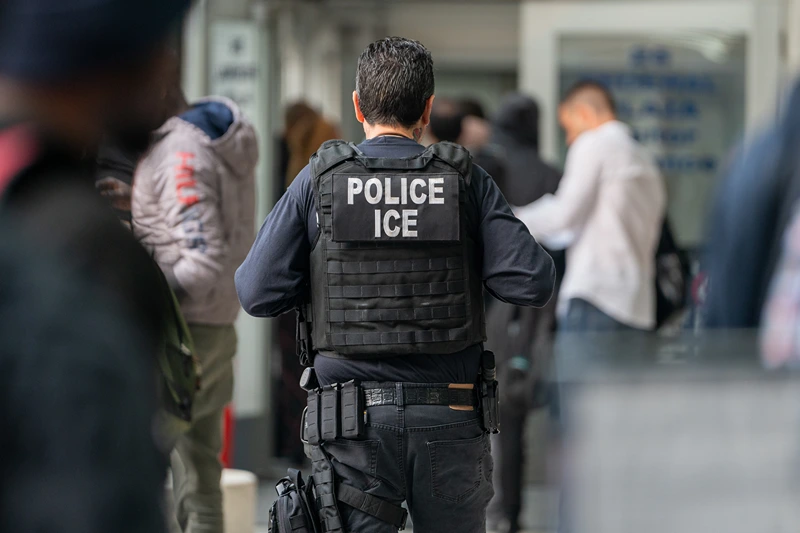 NEW YORK, NEW YORK - JUNE 6: An ICE agent monitors hundreds of asylum seekers being processed upon entering the Jacob K. Javits Federal Building on June 6, 2023 in New York City. New York City has provided sanctuary to over 46,000 asylum seekers since 2013, when the city passed a law prohibiting city agencies from cooperating with federal immigration enforcement agencies unless there is a warrant for the person