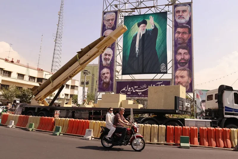 A man rides his motorcycle past a deactivated Kheibar Shekan ballistic missile in front of a picture of Iran's Supreme Leader Ayatollah Ali Khamenei in Tehran's Bahrestan Square on September 27, 2025, as part of an exhibit to mark the "Sacred Defense Week" commemorating the 1980-88 Iran-Iraq war. (Photo by ATTA KENARE / AFP) (Photo by ATTA KENARE/AFP via Getty Images)