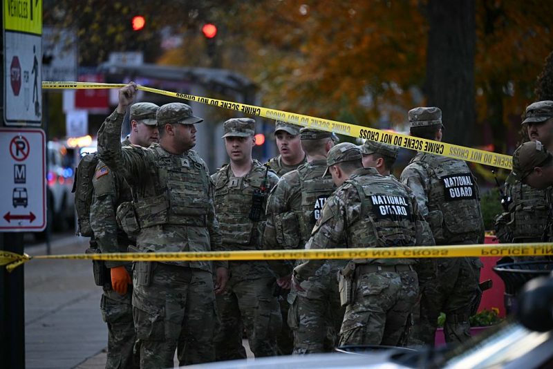 National Guard soldiers stand behind the crime scene tape at a corner in downtown Washington, DC, on November 26, 2025. Two National Guard soldiers were shot a few blocks from the White House, according to law enforcement. (Photo by Drew ANGERER / AFP via Getty Images)