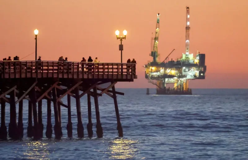 SEAL BEACH, CALIFORNIA - JANUARY 05: People stand on the the pier with offshore oil and gas platform Esther in the distance on January 5, 2025 in Seal Beach, California. President Joe Biden will reportedly permanently ban future offshore oil and gas drilling in over 625 million acres of federal waters in an effort to cement his environmental legacy before President-elect Donald Trump is inaugurated January 20th. Platform Esther is located approximately 1.5 miles away from Seal Beach and operates within California state waters. (Photo by Mario Tama/Getty Images)