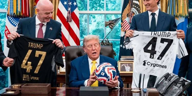 US President Donald Trump (C), flanked by Chairperson of Ferrari John Elkann (R) and FIFA President Gianni Infantino, holds a ball as he makes remarks in the Oval Office of the White House during a visit by members of Italian soccer club Juventus in Washington, DC, on June 18, 2025. Juventus will play Emirati club Al-Ain in the 2025 FIFA Club World Cup at Washington