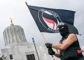 SALEM, OR - MARCH 28: A protester waves an anti-fascist flag at the Oregon statehouse on March 28, 2021 in Salem, Oregon. The protesters clashed with occupants of vehicles that had participated in an American flag-waving car caravan, despite law enforcements efforts to to keep the groups separate. (Photo by Nathan Howard/Getty Images)