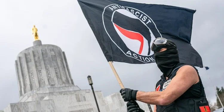 SALEM, OR - MARCH 28: A protester waves an anti-fascist flag at the Oregon statehouse on March 28, 2021 in Salem, Oregon. The protesters clashed with occupants of vehicles that had participated in an American flag-waving car caravan, despite law enforcements efforts to to keep the groups separate. (Photo by Nathan Howard/Getty Images)