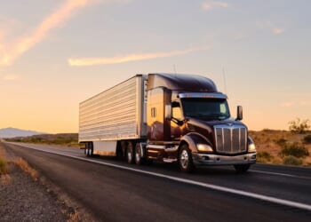 A large semi truck hauls freight down an open highway in the Western United States.
