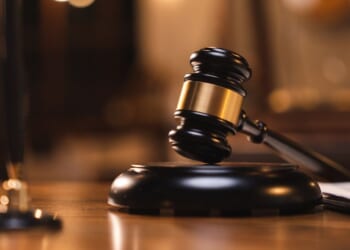 A judges gavel sits on a table as books sit in the background.