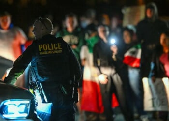A Department of Homeland Security agent stands guard as protesters demonstrate against recent raids conducted by the US Immigration and Customs Enforcement (ICE) outside the DHS office in Charlotte, North Carolina, on November 16, 2025. Federal immigration officers began immigration enforcement operations in Charlotte on November 15, they confirmed in a statement. "We are surging DHS law enforcement to Charlotte to ensure Americans are safe and public safety threats are removed," Assistant Homeland Security Secretary Tricia McLaughlin said. US President Donald Trump has made deporting undocumented immigrants a key priority for his second term, after successfully campaigning against an alleged "invasion" by criminals. (Photo by Peter Zay / AFP) (Photo by PETER ZAY/AFP via Getty Images)