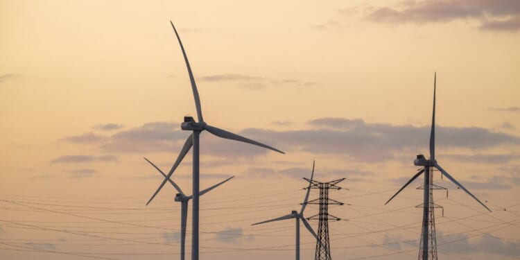 A wind farm with electricity pylons against the backdrop of an orange sky at the end of the day in Beauvilliers, France, on Nov. 25, 2025.
