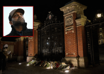 (Background) Brown University students and community members take a moment at a makeshift memorial for the victims of a December 13 mass shooting at the Van Winkle Gates outside Brown