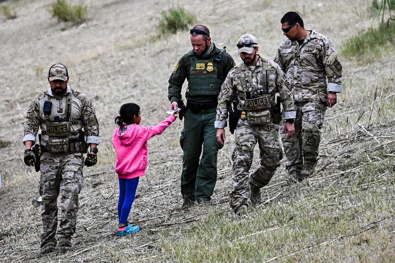 TOPSHOT - A US Customs and Border Protection officer gives food to an immigrant child waiting to be processed at a US Border Patrol transit center after crossing the border from Mexico at Eagle Pass, Texas on December 22, 2023. Texas Republican Governor Greg Abbott signed a bill on December 18, 2023 that would allow state police to arrest and deport migrants who cross illegally into the US from Mexico. (Photo by CHANDAN KHANNA / AFP) (Photo by CHANDAN KHANNA/AFP via Getty Images)