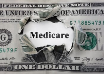“Torn U.S. dollar bill with the word ‘Medicare’ revealed through the rip.”