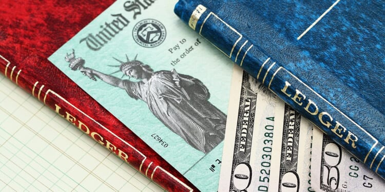An IRS tax refund check and several fifty dollar bills are showing between two account ledgers