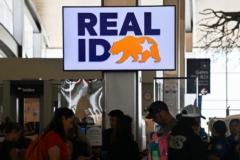 Travelers wait in line to pass through security and TSA screen under a sign reading "REAL ID" at Sacramento International Airport on May 15, 2025 in Sacramento, California. Real ID is a federally mandated form of identification in the US that meets enhanced security standards set by the Department of Homeland Security. Starting May 7, 2025, US residents will need a Real ID-compliant driver's license or identification card (or an acceptable alternative like a passport) to board domestic flights and enter certain federal facilities. (Photo by Robyn Beck / AFP) (Photo by ROBYN BECK/AFP via Getty Images)