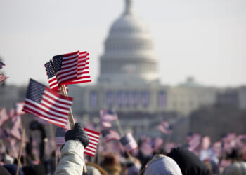 Crowd of people wave small American flags on the National Mall with the US Capitol in the background