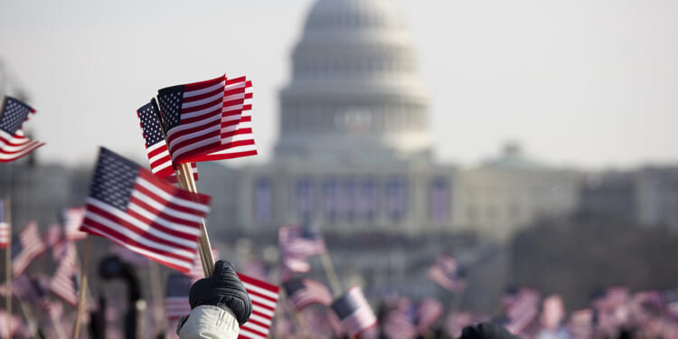 Crowd of people wave small American flags on the National Mall with the US Capitol in the background