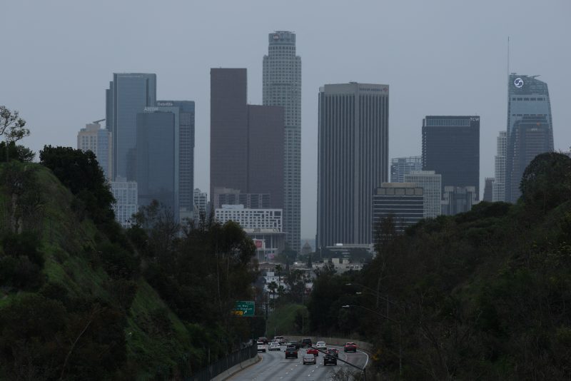 The downtown Los Angeles skyline stands on the horizon as vehicles drive on the 110 Freeway during a winter rain storm on New Years Eve in Los Angeles, California, on December 31, 2025, (Photo by Patrick T. Fallon / AFP via Getty Images)