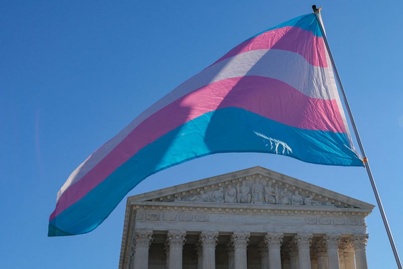 WASHINGTON, DC - JANUARY 13: Protesters supporting transgender athletes competing in women's sports wave a transgender pride flag outside the Supreme Court on January 13, 2026 in Washington, DC. Groups from both sides of the debate gathered on Tuesday morning to protest while two cases that prohibit transgender girls from joining girls' and women's sports teams are heard inside the Supreme Court. (Photo by Heather Diehl/Getty Images)