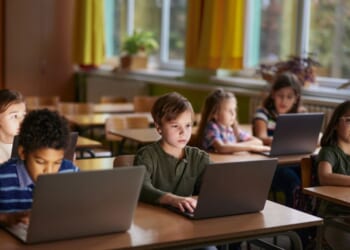 A large group of elementary students learning over laptops in the classroom.