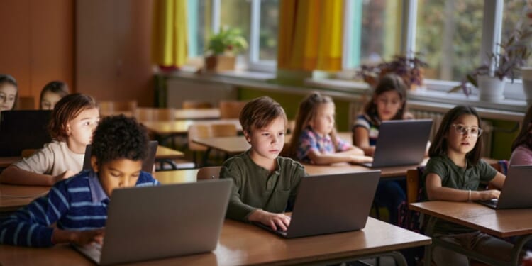 A large group of elementary students learning over laptops in the classroom.