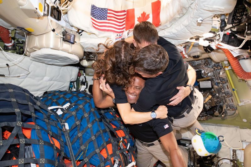 (April 7, 2026) – The Artemis II crew – (clockwise from left) Mission Specialist Christina Koch, Mission Specialist Jeremy Hansen, Commander Reid Wiseman, and Pilot Victor Glover – take time out for a group hug inside the Orion spacecraft on their way home. (Photo via NASA)