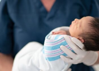 A nurse holds a newborn baby at a hospital as the child sleeps.