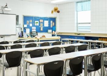 Chairs and desks sitting in rows in front of a whiteboard in a school classroom with no students.